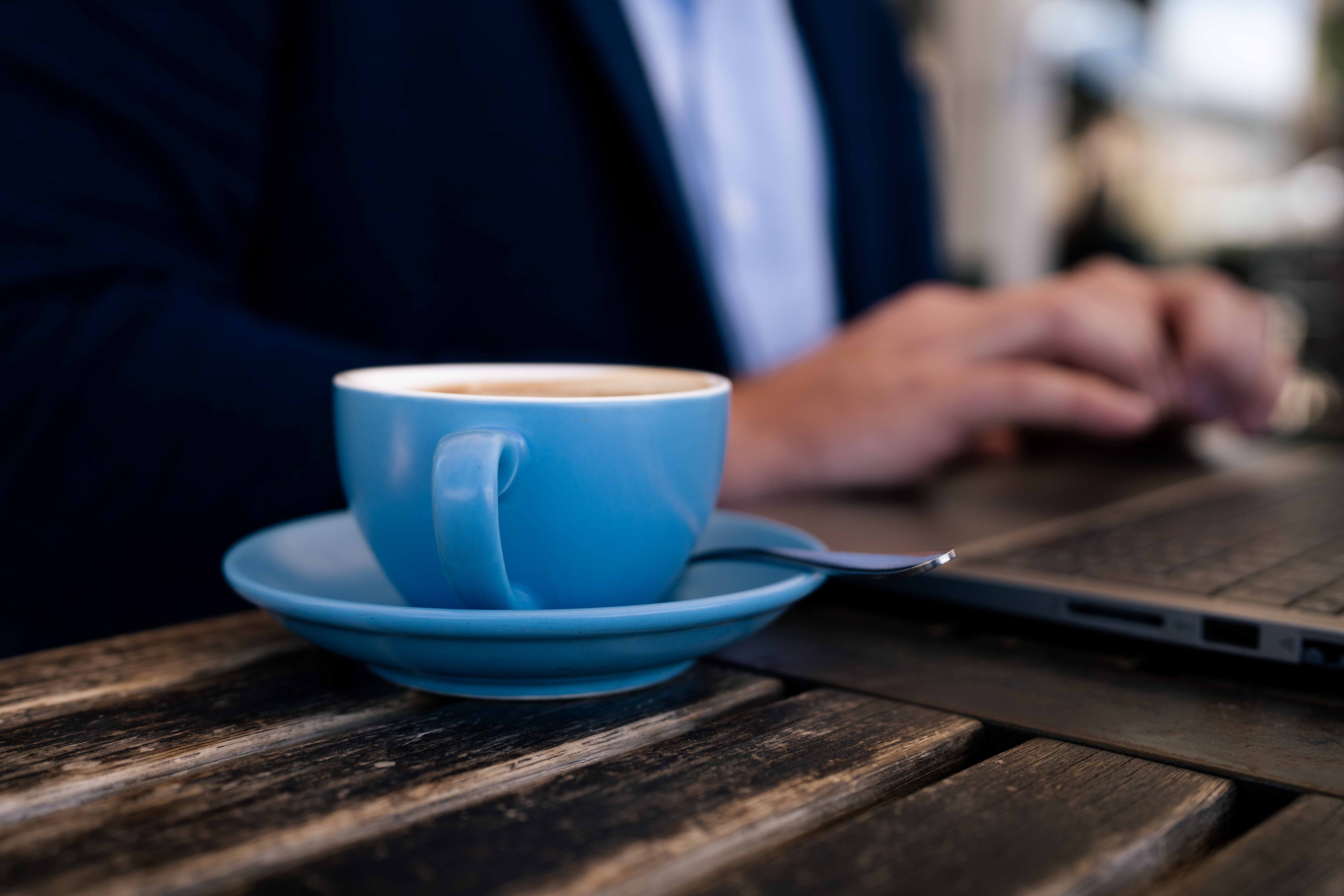Man working on a laptop at a cafe with a cup of coffee in a blue mug