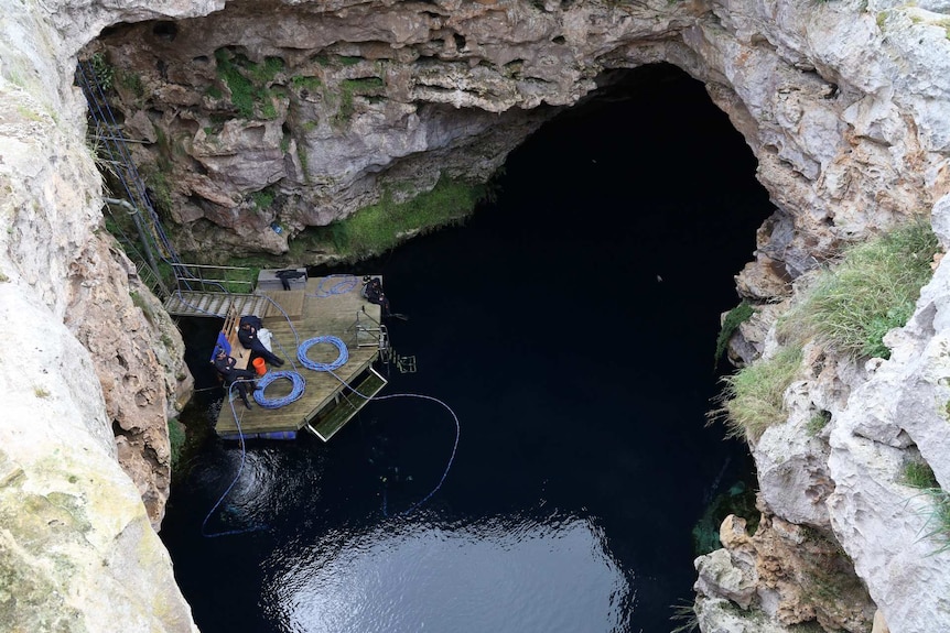 Three men on a platform on top of the water in a sinkhole.