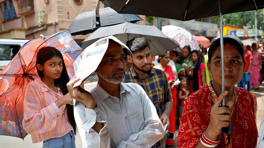 A man uses a newspaper as others use umbrellas to protect themselves from the heat.