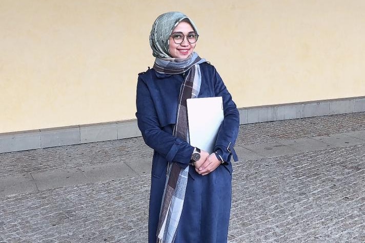 Woman wearing glasses and hijab smiling to camera.