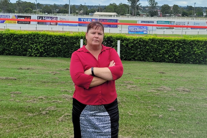 A woman wearing a red shirt stands with her arms crossed, looking at the camera.