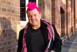 A man with spiky pink hair looks into the camera