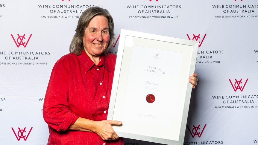 A woman in a red shirt holds a large framed certificate