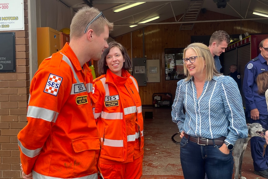 Jacinta Allan wears a blue and white striped shirt and jeans and talks to two SES workers in orange overalls.