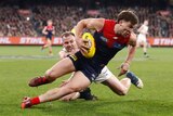 A Melbourne AFL player grimaces as he tries to break free of a tackle from behind.