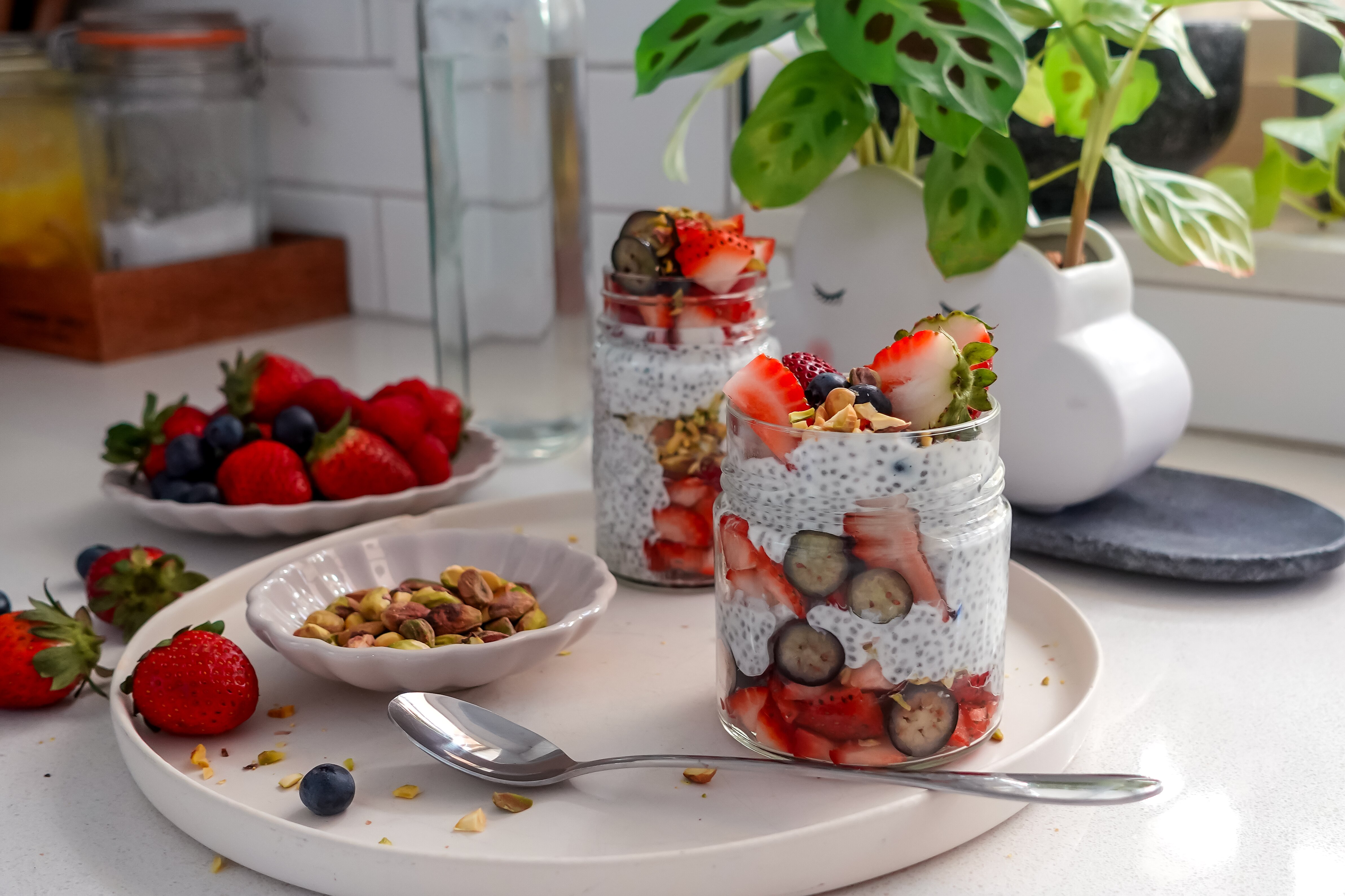 Dos vasos de pudín de semillas de chía con capas de fresas y arándanos y adornado con pistachos.