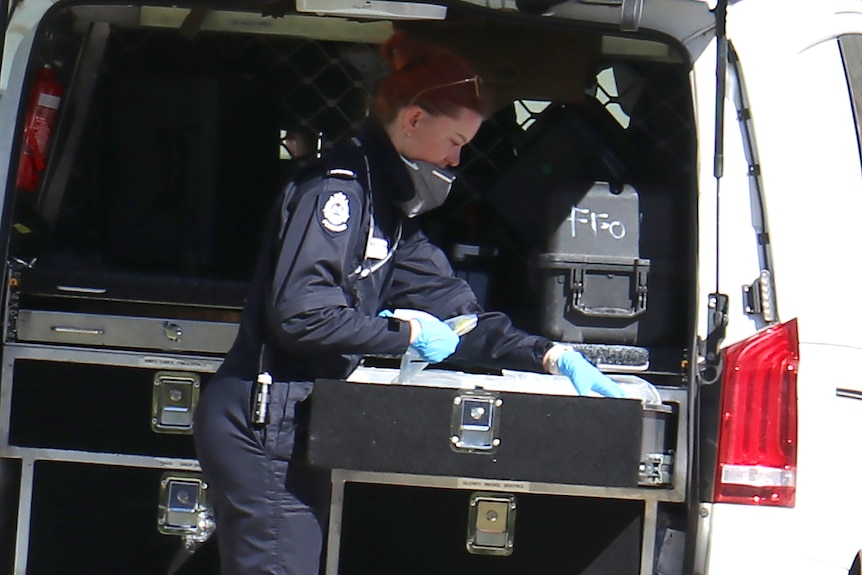 A close-up shot of a female police forensics officer at the back of a vehicle sorting through equipment.