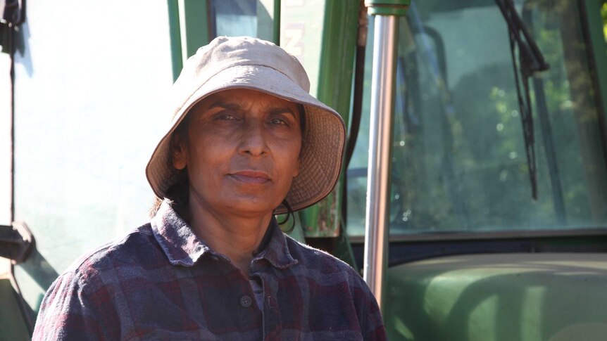 An Indian woman wearing a hat standing next to a tractor.
