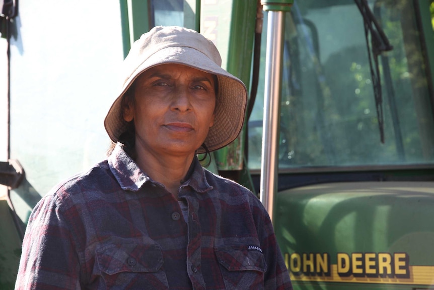 An Indian woman wearing a hat standing next to a tractor.