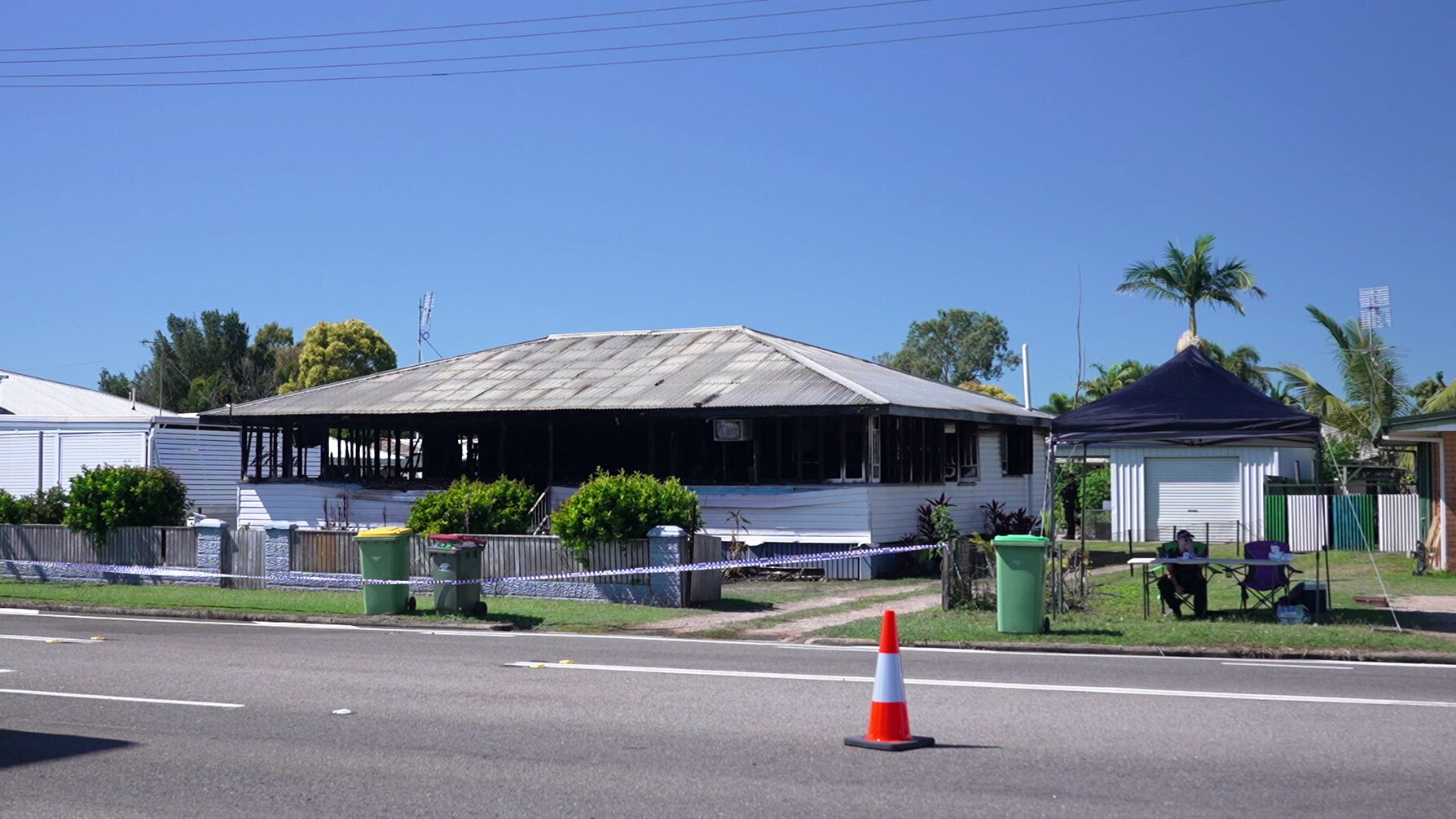 A burnt-out house surrounded by police tape with an officer sitting under a tent
