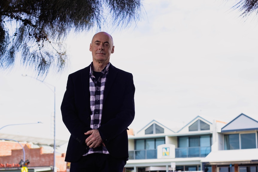 man in suit stands outside with houses in the background