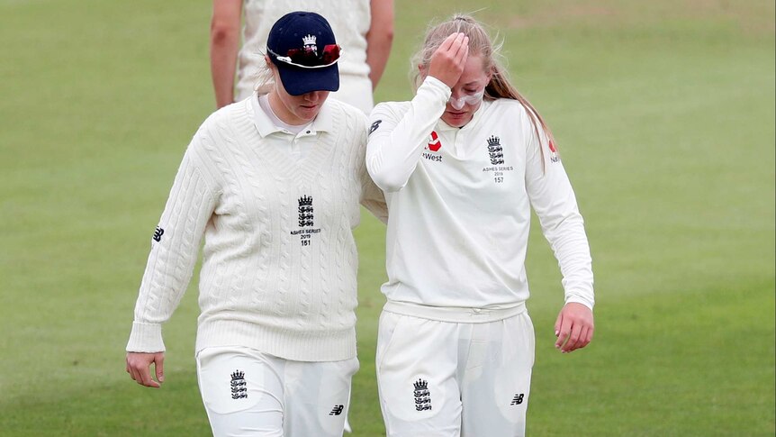 An England women's Test cricketer pats her teammate's back as she walks off the ground injured.