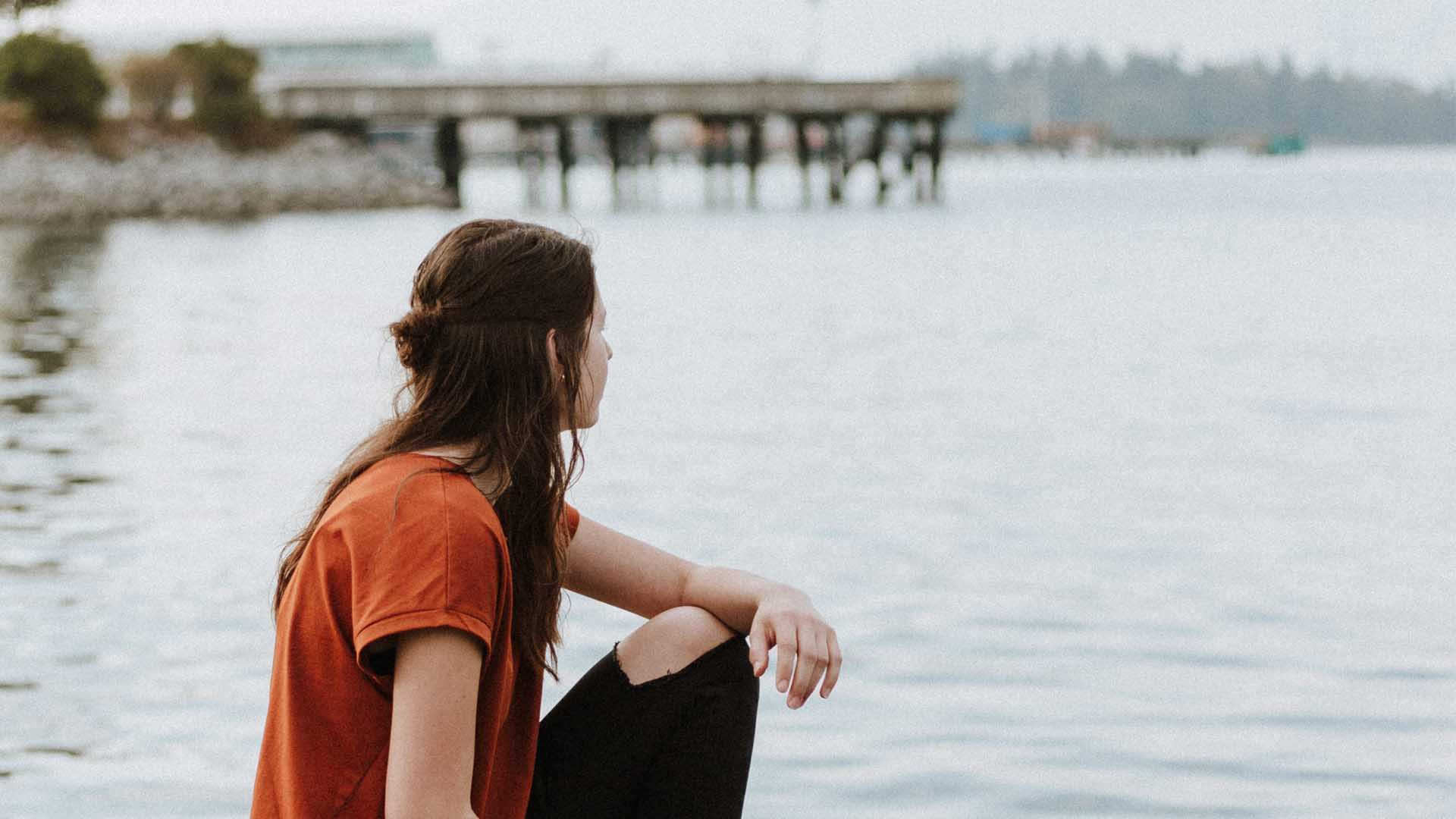 A woman who appears to be grieving looks over a lake, in a story about what not to say to someone who experience miscarriage.