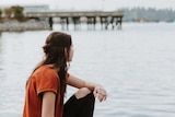 A woman who appears to be grieving looks over a lake, in a story about what not to say to someone who experience miscarriage.