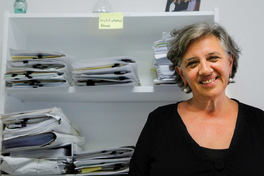 Women sitting stares toward camera, with files in background.