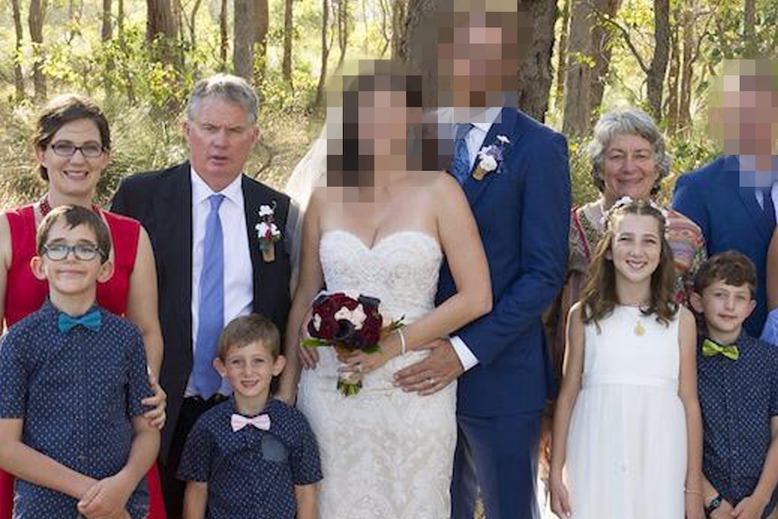 Family members pose for a wedding photo in front of trees and shrubs.