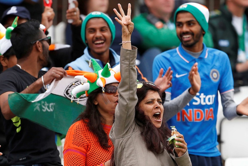 A women holds up four fingers while shouting during an Indian cricket match.