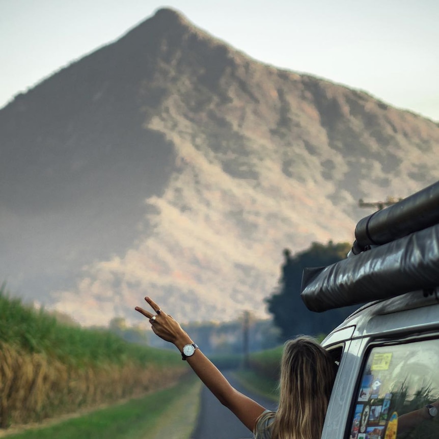 A person leans out of a van, traveling towards a mountain.