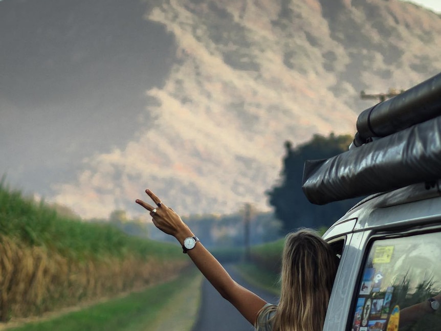 A person leans out of a van, traveling towards a mountain.