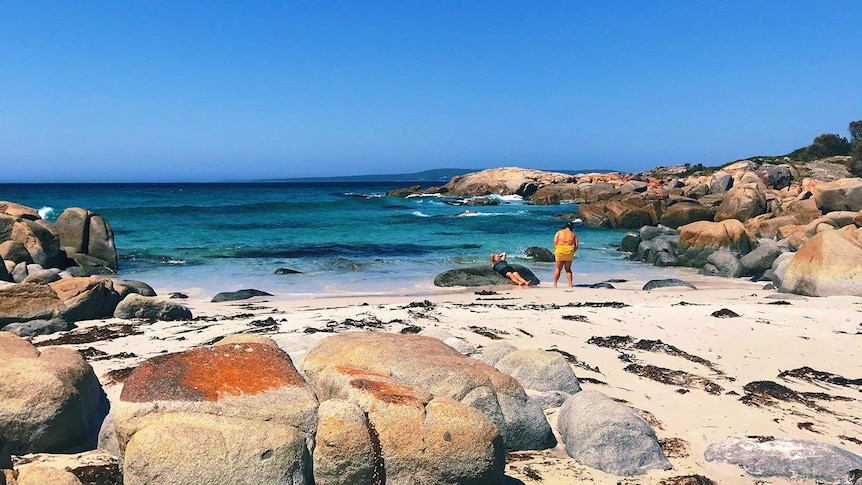 A woman stands on a beach surrounded by smooth stones