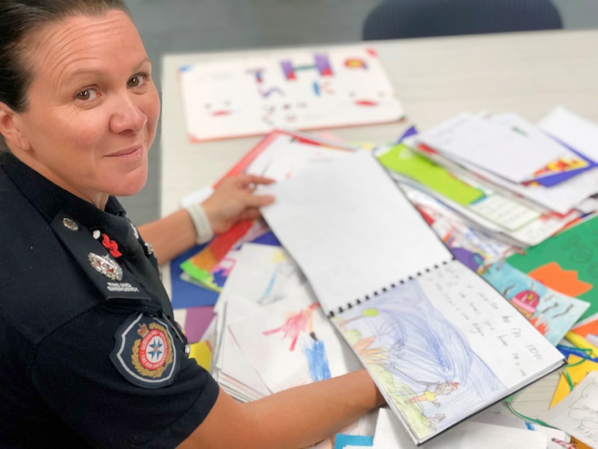 A female firefighter sits with a pile of hand-drawn artwork which children have created to say thank you.
