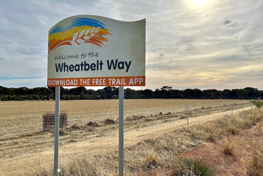 A sign reading 'Welcome to the Wheatbelt Way' stands alongside a road with a dry field
