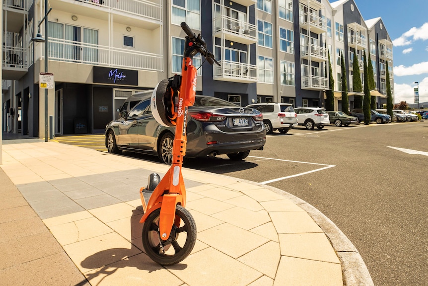 An orange e-scooter parked on a footpath.