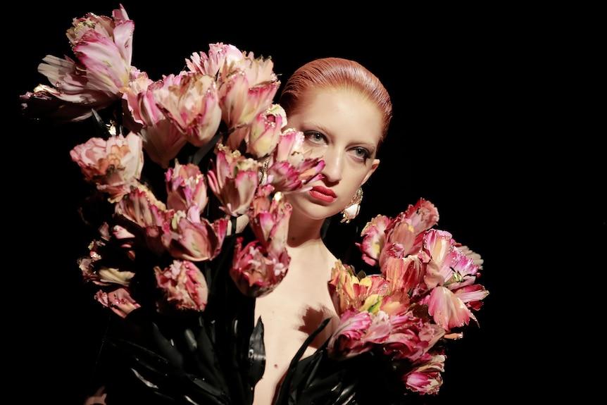 A model wearing a shirt made from pink flowers which are as high as her head. 