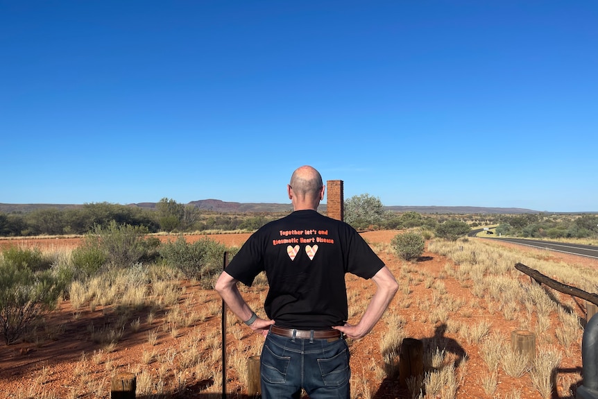 Balding man in black t-shirt with hands on his hips with his back to the camera, looking out over the desert landscape.
