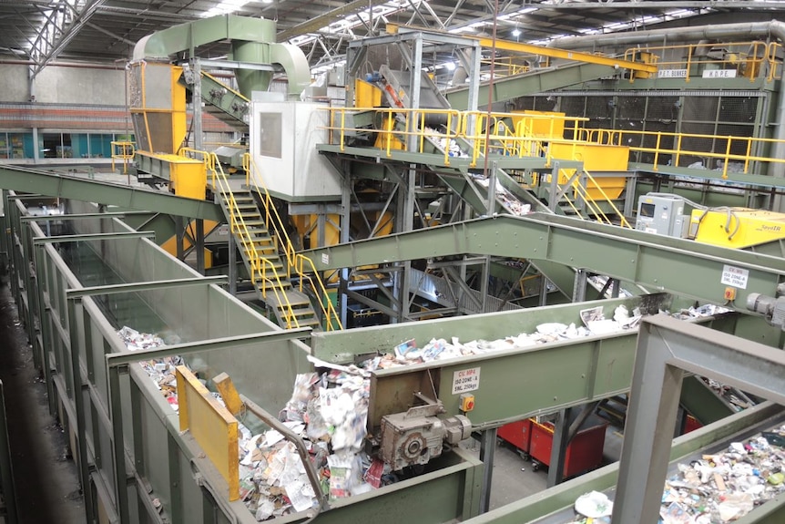 A large green and yellow conveyor belt full of recycling.