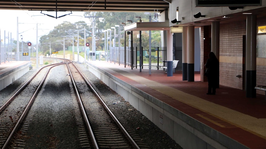 Thornlie train station showing train tracks and platform with just one woman standing on it.