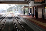 Thornlie train station showing train tracks and platform with just one woman standing on it.