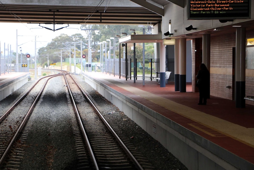 Thornlie train station showing train tracks and platform with just one woman standing on it.