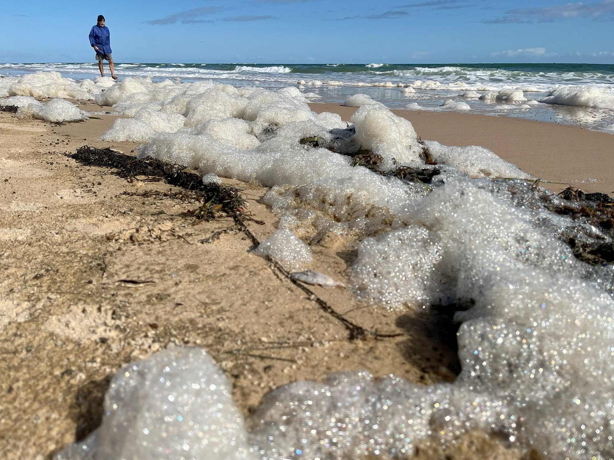 Sea foam on a beach with a man walking in background