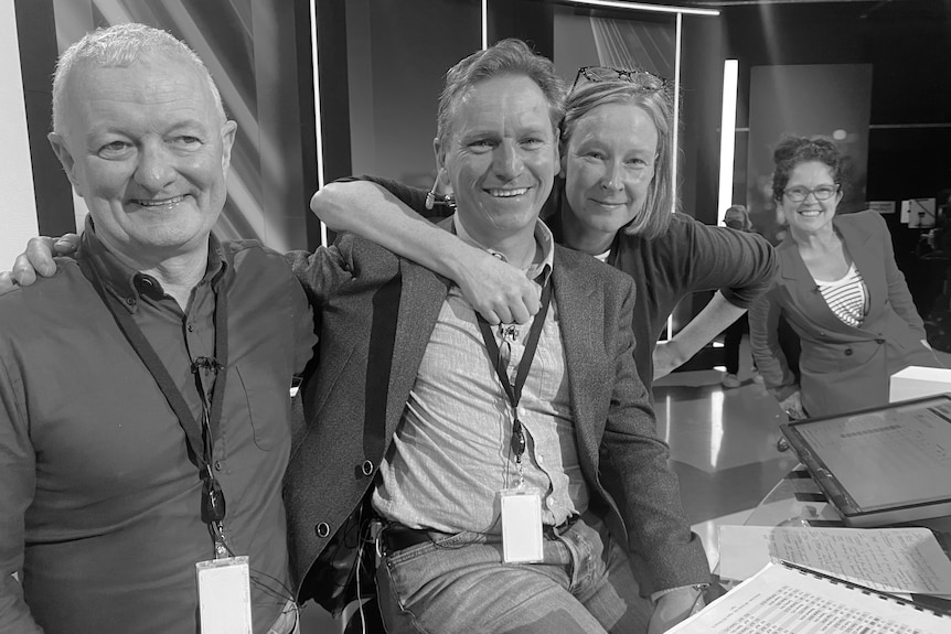 Black and white photo of four people arms around each other sitting on set.