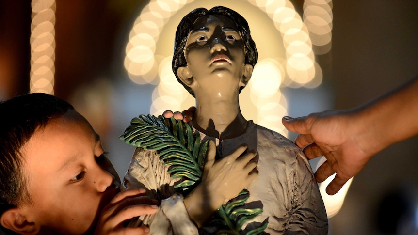 A boy kisses a statue of Pedro Calungsod, the new patron saint for young people.