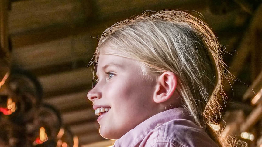 A young girl stares out the side of the picture smiling.