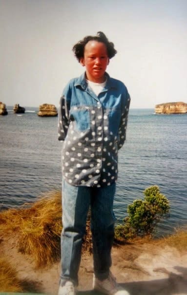 Carly stands in front of the ocean, wearing a denim outfit. 