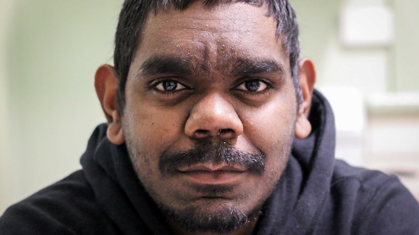 A 23-year-old man wearing a black hoodie looks into the camera.