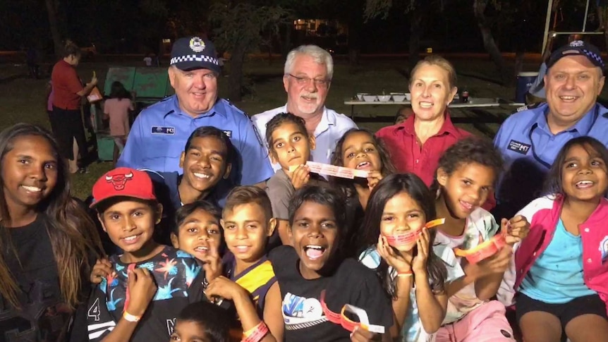police officers and other adults standing in a group with a dozen Aboriginal children.