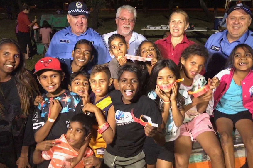 police officers and other adults standing in a group with a dozen Aboriginal children.