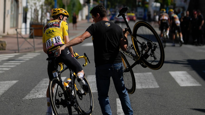The Tour de France leader leans to get off his bicycle as a team worker carries a replacement bike over his shoulder. 