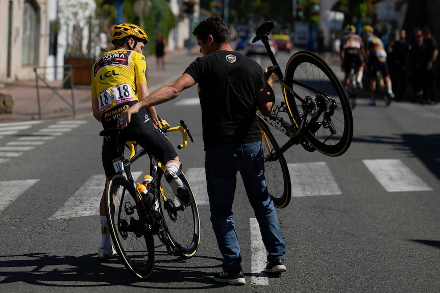 The Tour de France leader leans to get off his bicycle as a team worker carries a replacement bike over his shoulder. 