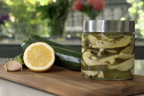 Zucchini slices in a pickle jar on a table next to a lemon cut in half.