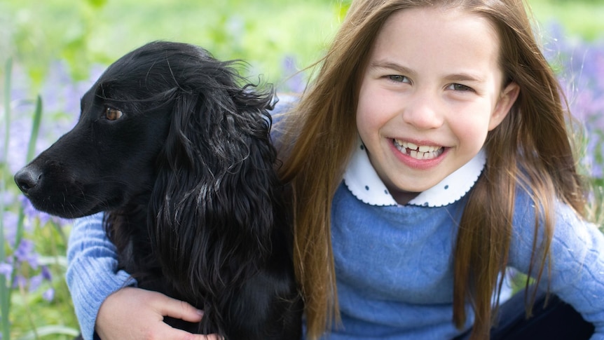 A girl in a field smiles with her pet dog