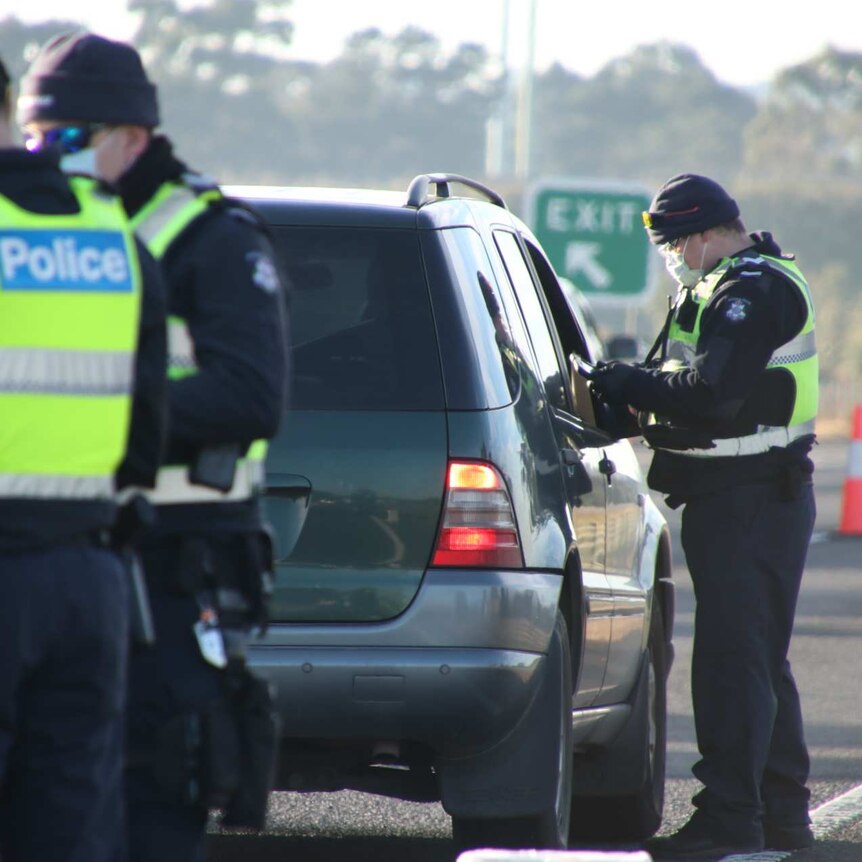 Three police officers at a coronavirus checkpoint on a highway.