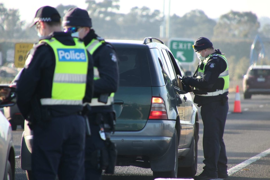 Three police officers at a coronavirus checkpoint on a highway.