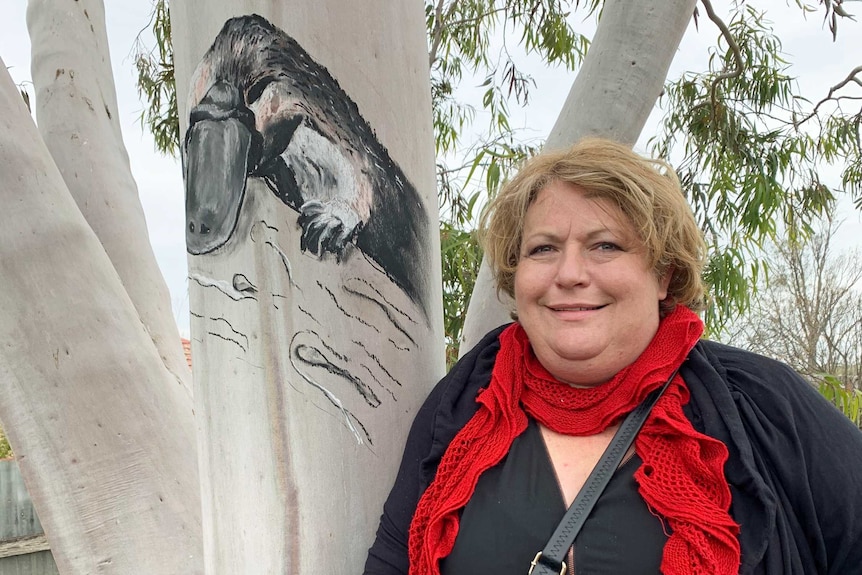 A woman stands next to a painting of a platypus on a tree