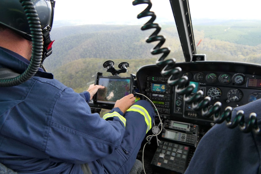 A view from behind a pilot in a helipcopter looking down onto bushland.