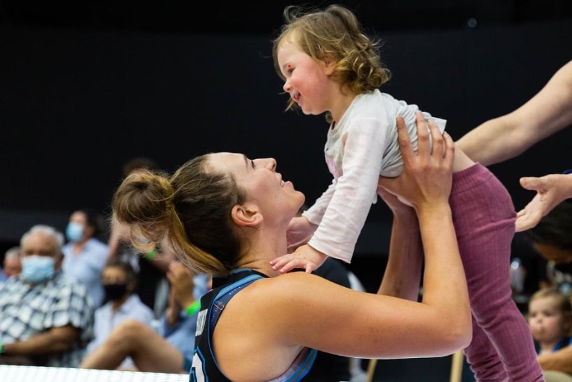 Alex Bunton holding her daughter up above her head while standing on a basketball cout. 
